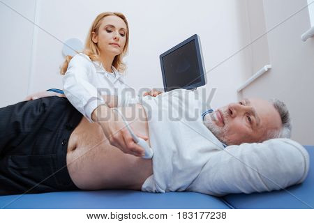The process of ultrasound tumor detection. Involved female cheerful medic working in the hospital while providing ultrasonic body monitoring and using ultrasound machine