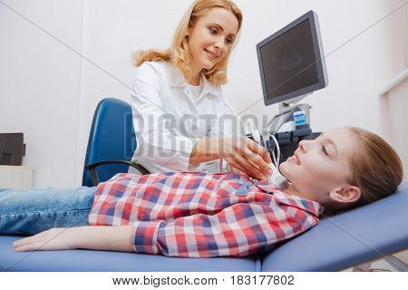 Waiting for positive analysis result. Smiling positive young patient lying on the medical couch and enjoying visit to the sonographer while medical specialist providing ultrasonic thyroid scanning
