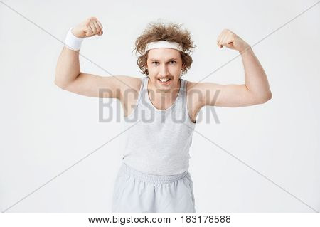 Old-fashioned style. Man in grey retro sportswear demonstrates biceps, showing teeth looking at camera