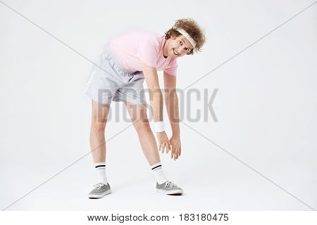 Sporty man stretching back and leg muscles looking straight with funny face. Retro photography style
