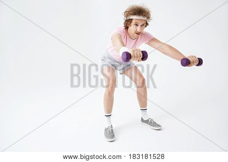 Man doing squats, holding light dumbbells. Isolated on grey background. Sport and health concept