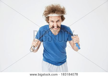 Closeup of young man in sport outfit biting jumping rope, looking straight at camera