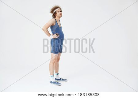 Side shot of man in blue jumpsuit, long white socks. Guy with belly looking upset