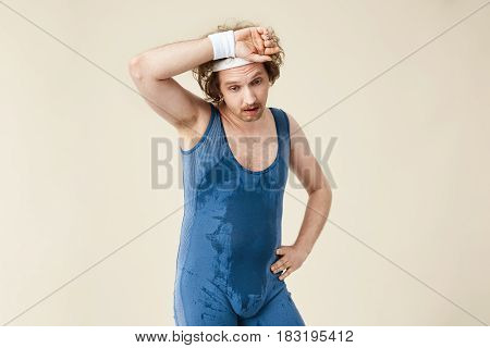 Tired man in wet and sweaty jumpsuit mopping his brow after hard work out.