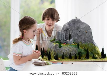 Children work on model building school project. Kids build miniature scale model mountain for geography class. Extracurricular activities and hobby club. Art and crafts for teenager and preschool.