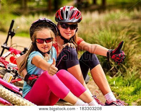 Mother and daughter on bicycle. Bikes cycling family. Happy mother and daughter are sitting on green grass road near bicycles. Cycle racing concept.