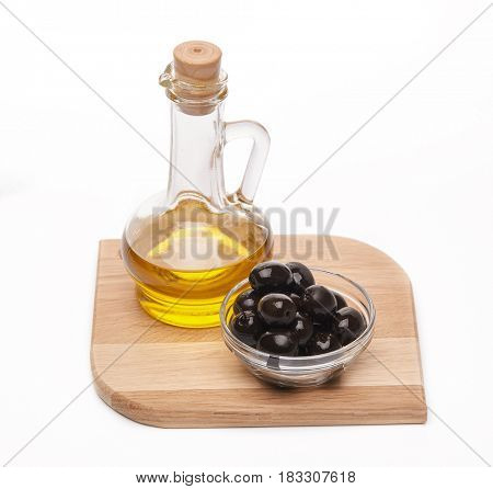 Glass cruet with Extra virgin olive oil, canned black olives in bowl stand on a wooden cutting board on a white background.