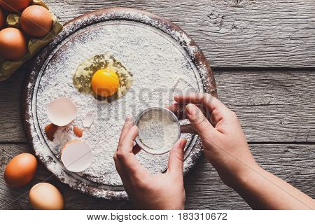 Baking concept. Yands sift sprinkled flour and eggs on wooden cutting board near knife, cooking ingredients. Prepare for making yeast dough. Top view, copy space