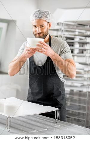 Handsome cheese maker in uniform forming cheese into molds at the small producing farm