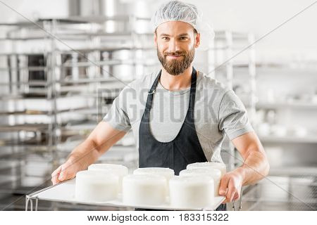 Handsome cheese maker in uniform forming cheese into molds at the small producing farm