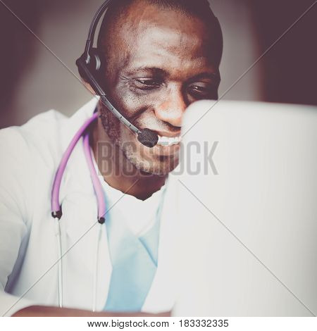 Portrait of young male doctor wearing headset while using computer at desk in clinic.