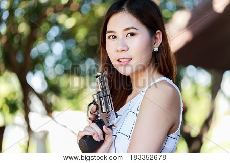Side view of young pretty Asian woman, in casual outfit, holding a hand gun, blur background