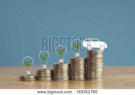 pile of money coins with small green tree light bulb and paper car on wood and soft blue background concept in fiance loan and buying