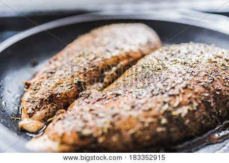 Barbecue fillet of chicken breast in Provencal herbs paprika black pepper in a black frying pan.