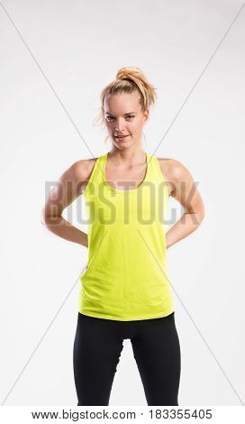 Attractive young fitness woman in yellow tank top. Studio shot on gray background.