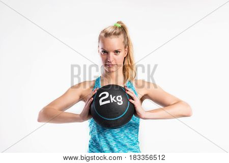 Attractive young fitness woman in blue tank top, holding medicine ball. Studio shot on gray background.