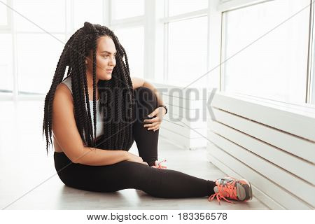 What a great day. Dreamy stunning glamorous lady looking out of the window while resting on the floor after having a nice workout in gym