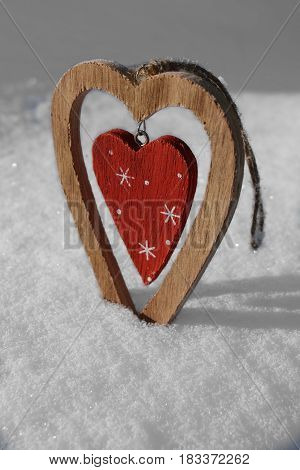 Vintage wooden heart which is in the middle of another wooden heart in red with snowflakes standing in the snow and drops beautiful shadow