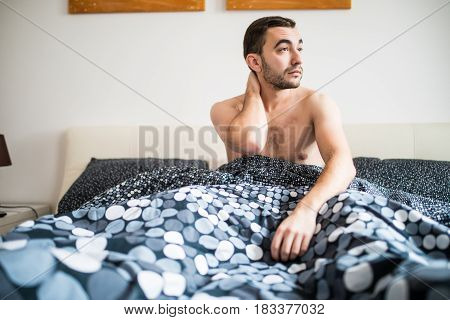 Young Man Suffering From Neckache In Bedroom At Home