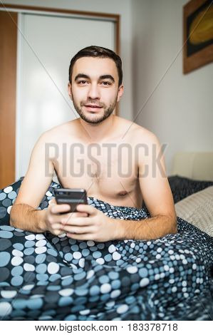 Bearded Man Lying In Morning Bed With Phone Using App Or Reading News Feed