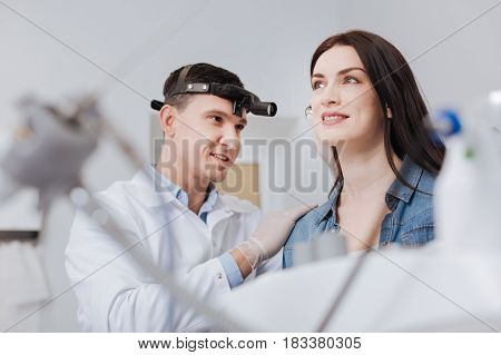 I am confident. Handsome doctor looking at his patient putting ear-funnel into her ear while expressing positivity