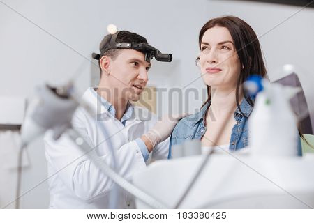 Bad feelings. Delighted doctor being well equipped examining ear of his visitor while using ear-funnel