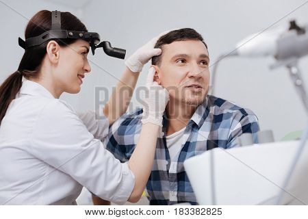 Great job. Delighted female wearing ENT head light putting ear-funnel into male ear sitting in semi position