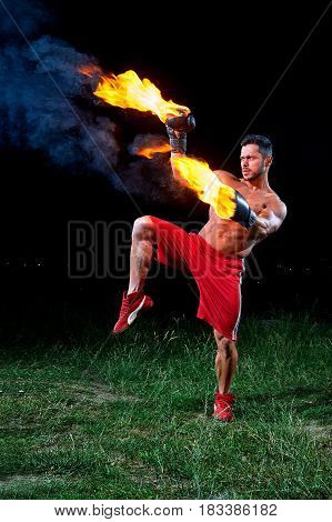 Vertical shot of a muscular aggressive fighter with burning boxing gloves training outdoors at night fire fiery flaming burn power strength sports fierce masculinity motivation effort energy.