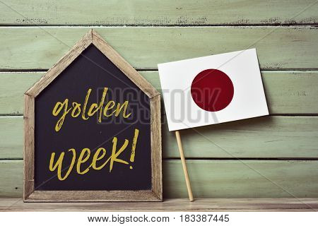 a house-shaped blackboard with the text golden week written in it and a flag of japan, against a pale green rustic wooden background