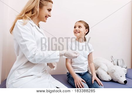 Need to consult. Beautiful young nurse keeping smile on her face holding thermometer in right hand while sitting in semi position