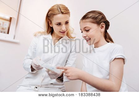   Confident family doctor keeping smile on her face sitting close to little girl while explaining the prescription