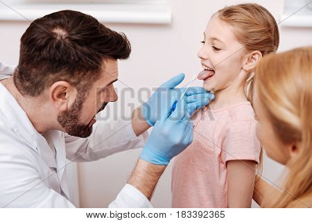   Funny girl standing opposite her pediatrician showing her tongue while checking her health