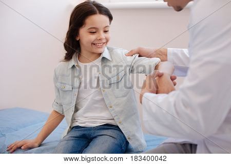 Doctor checkup. Cheerful positive cute girl sitting on a couch and being examined by a rheumatologist while visiting a hospital