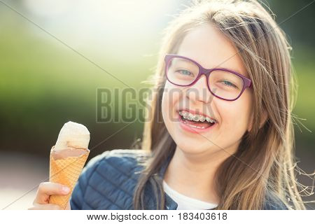 Girl. Teen. Pre teen. Girl with ice cream. Girl with glasses. Girl with teeth braces. Young cute caucasian blond girl wearing teeth braces and glasses. Portrait of a smiling young girl.