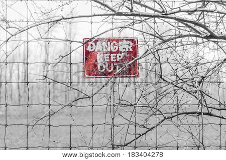 Red Danger sign posted to barbed fence tangled in branches warning people to keep out. Sign in middle with red color isolated.
