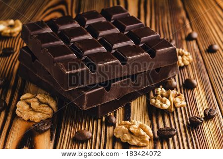 Three pieces of bitter dark chocolate bar walnut core and coffee bean on wooden background close-up view.