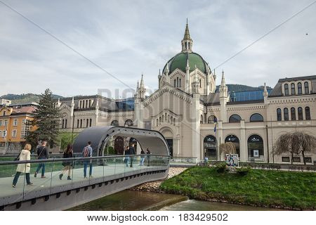SARAJEVO BOSNIA HERZEGOVINA - APRIL 16 2017: People walking in front of the Academy of fine arts of Sarajevo (Akademija likovnih umjetnosti ) crossing a bridge on Miljacka river.