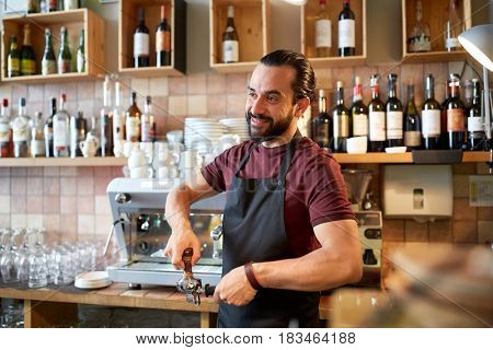 small business, people and service concept - happy man or waiter in apron with holder and tamper preparing espresso at coffee shop