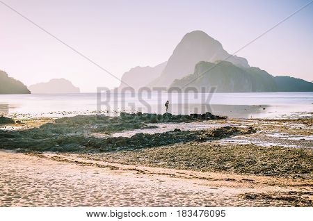 Lonely photographer on top of the rocks during low tide making photo on morning sunrise light in front of amazing Cadlao Island, El-Nido, Palawan, Philippines.
