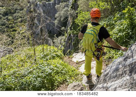 Back view of male climber in outfit using mountaineering equipment for via ferrata
