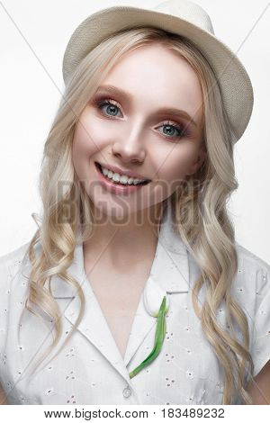 Young smiling girl with curls in a hat. A beautiful model in a white shirt and a brooch-flower. Gentle makeup. Summer light image. Beauty of the face.