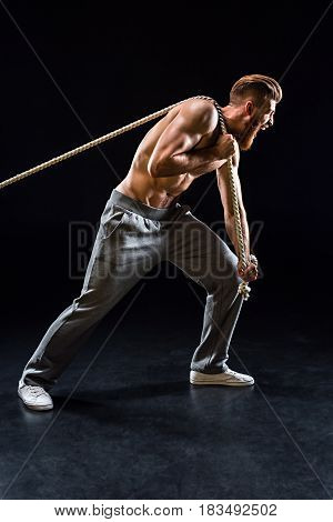 Handsome Bearded Sportsman Yelling And Pulling Rope Isolated On Black