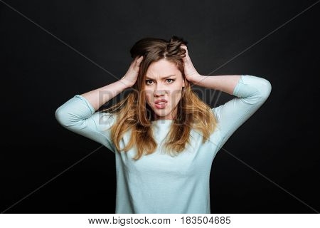 Feeling undisguised aversion. Annoyed emotional young woman expressing fury and touching her head while gesticulating wildly and standing isolated in black background