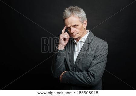 Feeling discomfort. Thoughtful involved aged man thinking while touching his forehead and standing against black background