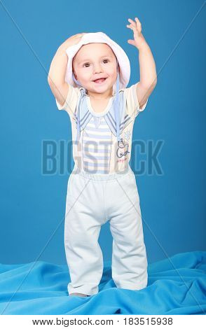 The kid in the sailor suit standing there smiling raising his hand to the top. Blue background