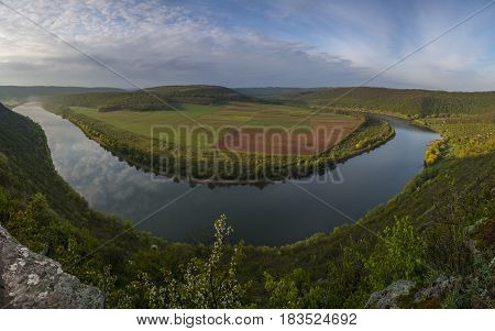 Dnestr (Dniester) river top view in springtime. The river surrounds multicolored field. Mountains slopes are covered with lush bright green vegetation.