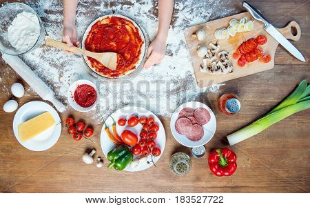 Top View Of Child Making Pizza With Pizza Ingredients, Tomatoes, Salami And Mushrooms On Wooden Tabl