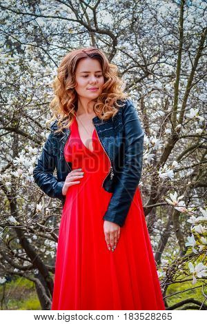 Young beautiful caucasian woman in blooming spring garden of magnolias . The girl in the garden on a cloudy day .