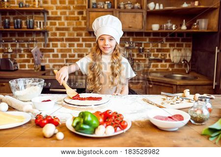 Smiling Girl In Chef Hat Putting Tomato Sauce On Pizza Dough