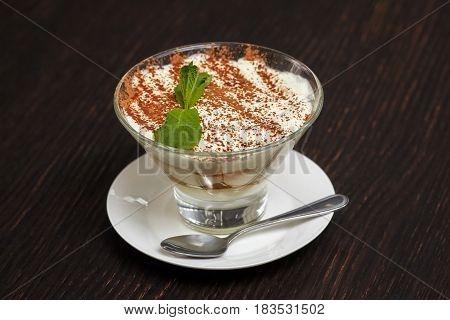 Tiramisu creme cake dessert in glass with mint leaves on black wooden background